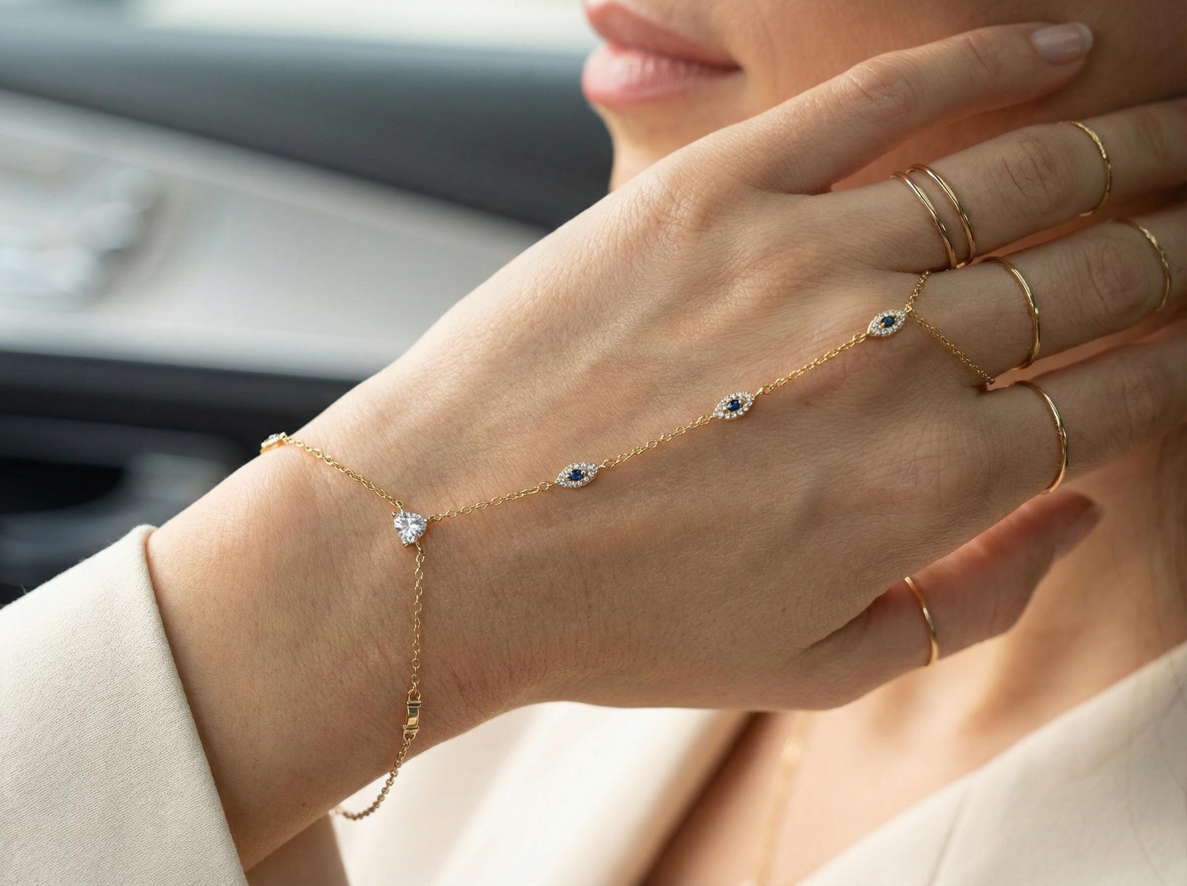Close-up detail of 14k gold evil eye hand chain bracelet showing small blue sapphire style stones and heart shaped diamond accent on thin delicate chain.