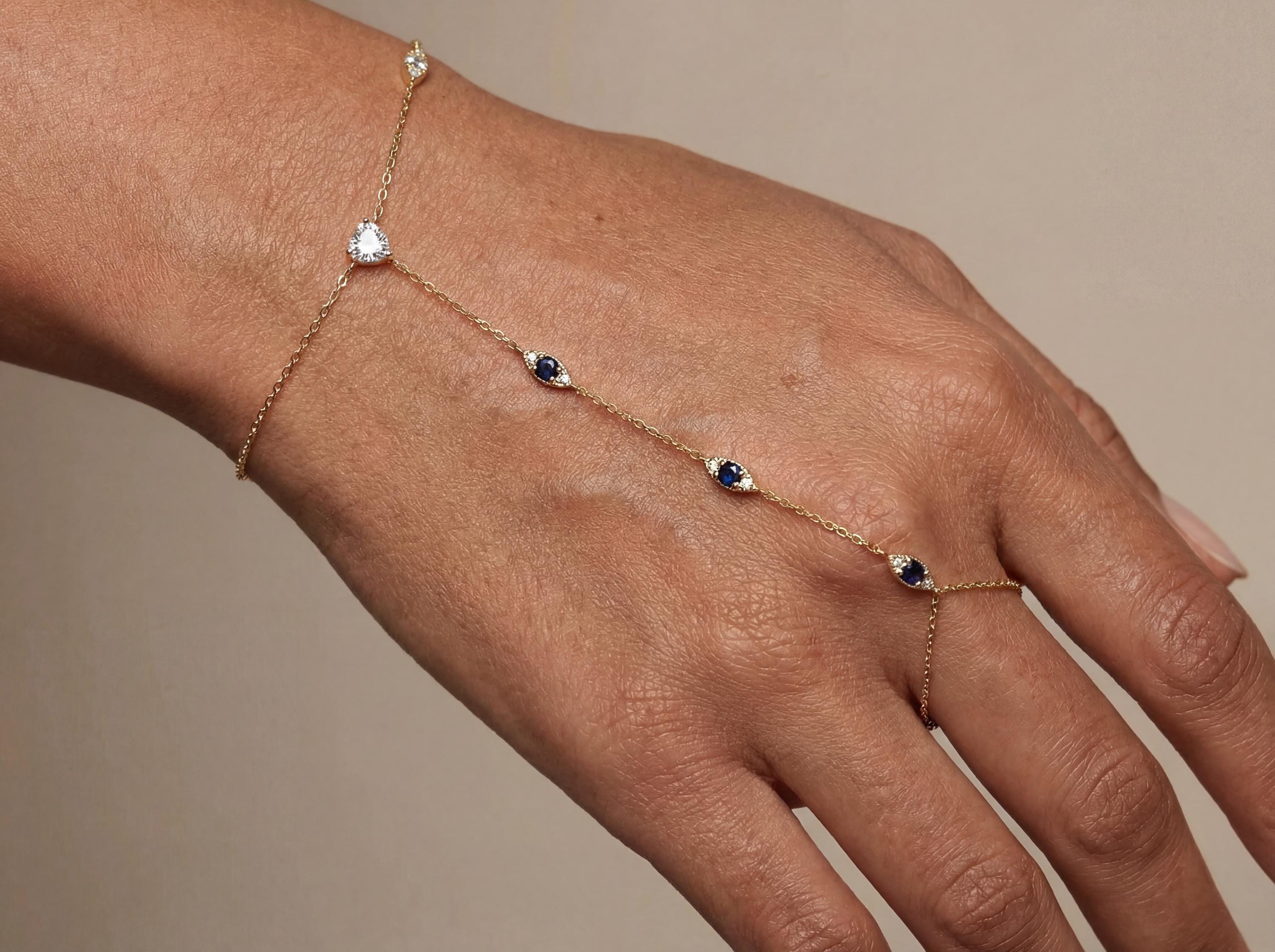 Delicate 14k gold evil eye hand chain bracelet placed on jeweler workbench with tools and design sketch, showing handmade fine jewelry process and thin gold chain details.