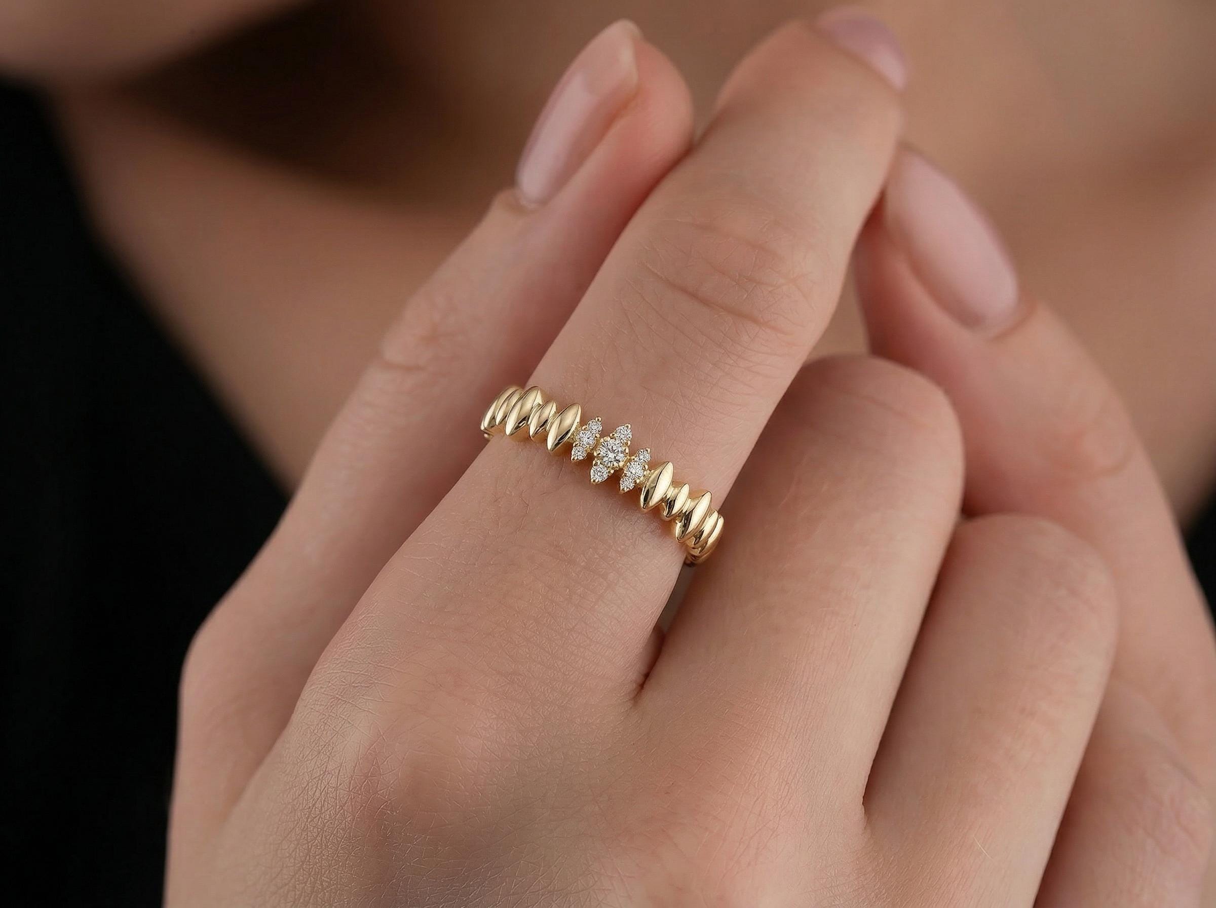 Close-up of textured gold wave band with small diamond cluster center, worn on finger, showing sculptural shape and polished finish.