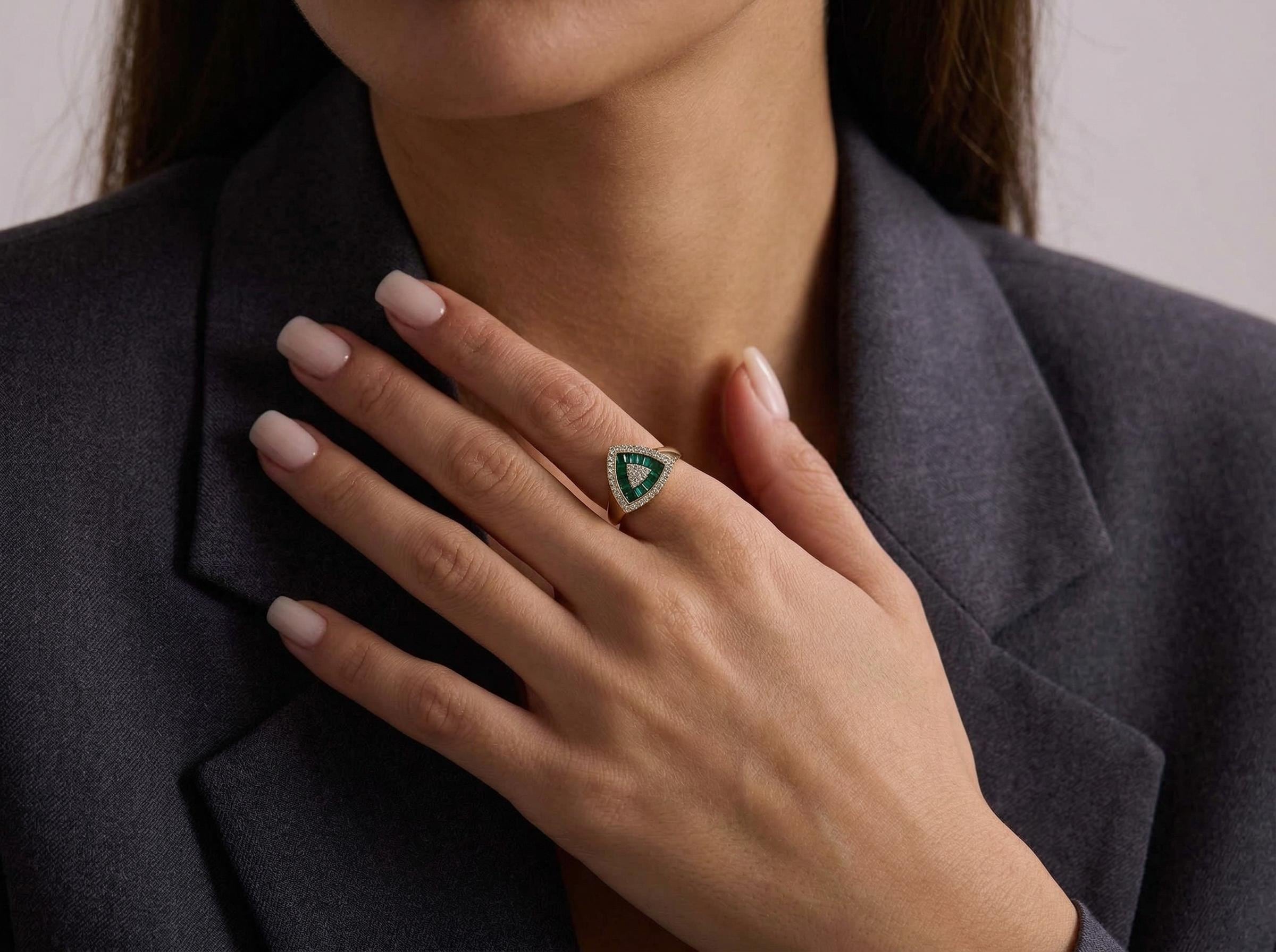 Emerald baguette triangle ring worn on hand, geometric fine jewelry design in solid 14k gold with diamond halo setting. Close view showing elegant proportions and refined style.
