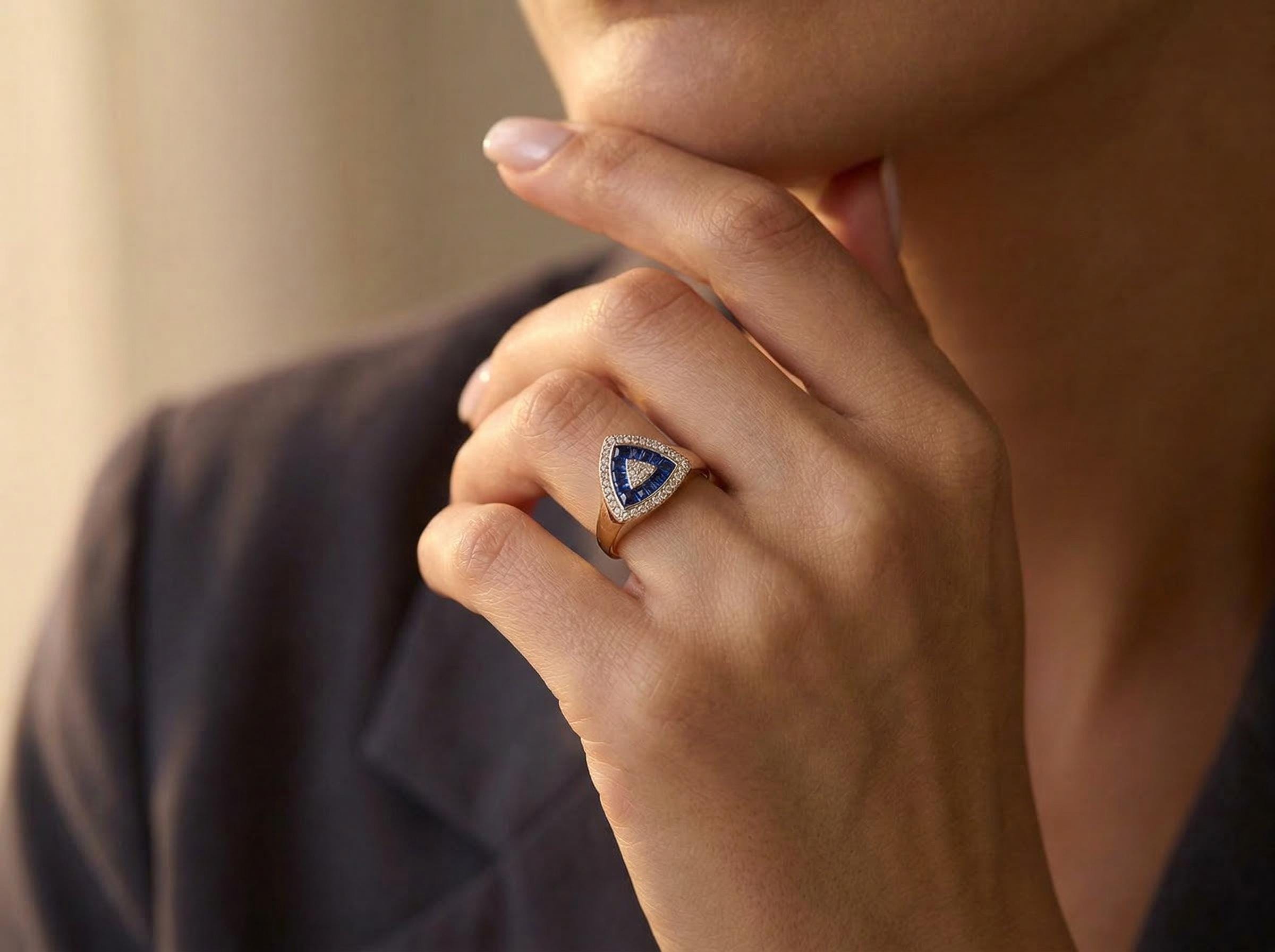 Close view of sapphire baguette triangle ring on finger, showing diamond halo setting and geometric stone arrangement in solid 14k gold.